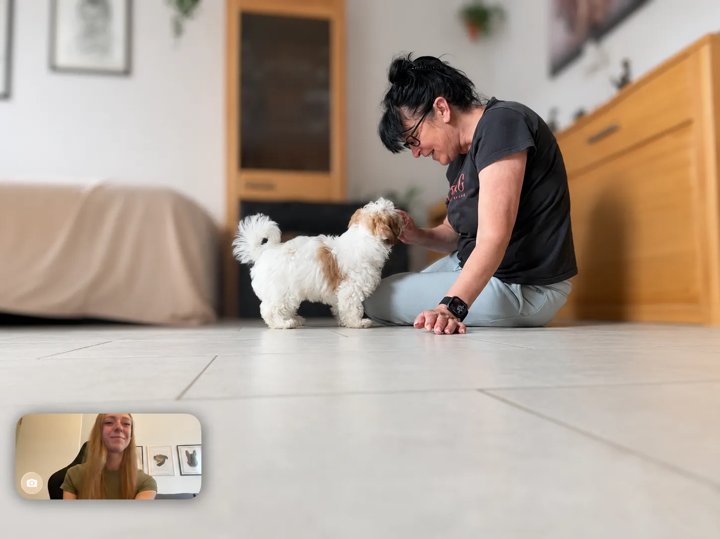 Hundehalterin sitzt mit ihrem Welpen zu Hause auf dem Boden, Lisa Trinkaus ist im Videofenster zum Coaching zugeschaltet